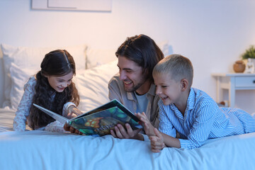 Father reading book for his children in bed