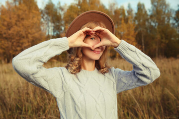 Beauty portrait of stylish happy young woman showing heart gesture, girl smiling in autumn park