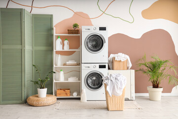 Two washing machines, dryer, shelving unit and baskets with clothes in interior of home laundry room