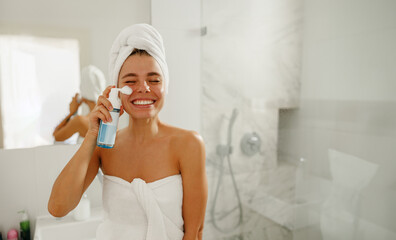 A joyful woman is having a great time as she enjoys her elaborate skincare routine in a chic,...