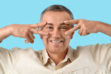 Obraz premium Happy mature man doing face building exercise on blue background