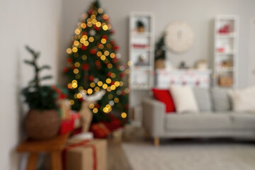 Interior of festive living room with grey sofa, glowing Christmas tree and shelving units, blurred view