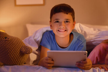 Cute happy little kids with tablet playing video games in evening at home