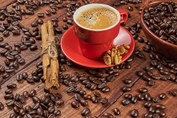 Cup of coffee in the foreground with roasted coffee beans and a cinnamon stick against a background of old wood