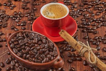 Cup of coffee in the foreground with roasted coffee beans and a cinnamon stick against a background of old wood