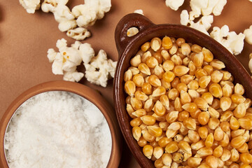 Golden corn kernels in a rustic ceramic container, the main ingredient for preparing crunchy popcorn, accompanied by a jar of salt