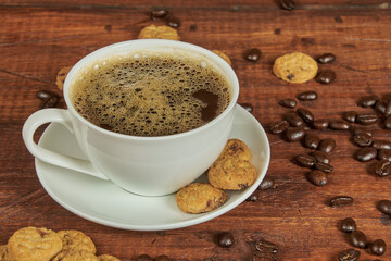 Cup of delicious gourmet coffee accompanied by crunchy cookies and roasted coffee beans on an old wooden background