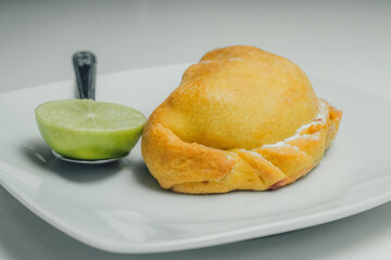 Empanas de harina, en plato blanco, acompañado de medio limón, sobre fondo blanco.