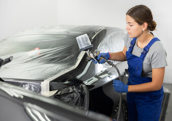 Car painting and automobile repair service. Female auto mechanic in blue overalls paints car with...