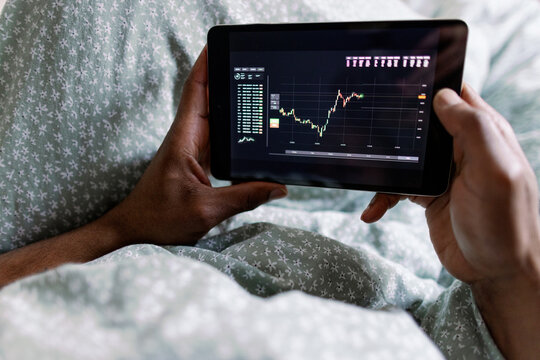 Partial black man watching graph on digital tablet lying on bed