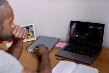 Cropped adult black man watching stock market graph on laptop