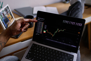 Cropped man pointing with finger at stock market graph on laptop