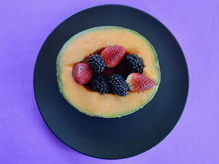 A cantaloupe with delicious strawberries and blackberries on a plate.