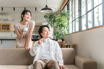 家のリビング・ソファで会話する仲良しの若い日本人夫婦
