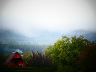 A beautiful red cabin surrounded by mountain giants with rain setting down upon them.