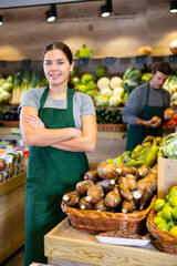 Portrait of friendly woman seller in an apron against the background of fruits and vegetables in a...