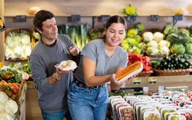 Couple of man and woman buying packaged carrots and sliced papaya in fruit shop