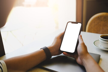 Person holding a smartphone with blank screen at a table with a coffee cup. Mockup for mobile app and design.