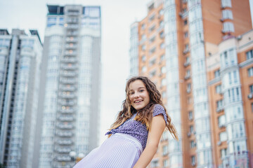 Fototapeta premium Pretty girl in casual clothes against the background of a metropolis street and a skyscraper. View from below
