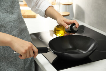 Woman with bottle of oil and frying pan in kitchen, closeup