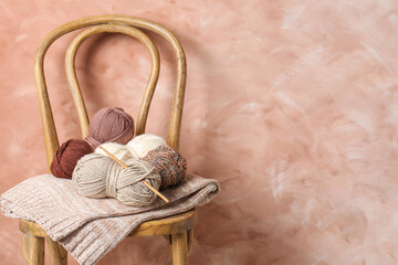 Different yarns, crochet hook and project on chair near beige wall. Space for text