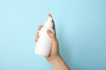 Woman with shampoo bottle on light blue background, closeup