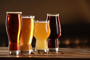 Glasses with different types of beer and pistachio nuts on wooden table indoors