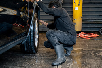 Man Squatting and Polishing a Black Car Tire with a Sponge at a Car Wash