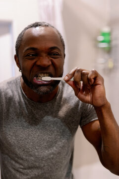 Adult black man looking at himself in mirror during brushing teeth