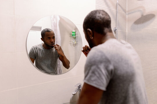 Back view of black man brushing teeth with toothbrush in bathroom