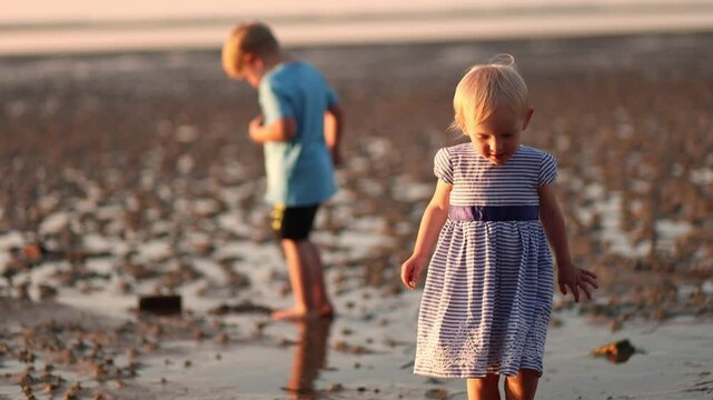 Two children walking barefoot on wet sand during low tide