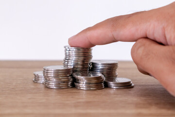 Man stacking and counting coins on the wooden table with white background. Savings or investment concept.