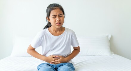 Obraz premium Woman Sitting on Bed Holding Stomach in Pain
