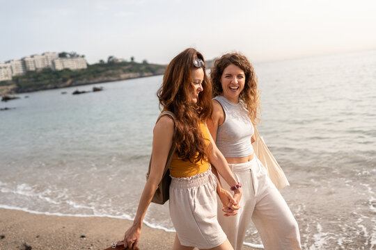 Two women holding hands walking on the beach