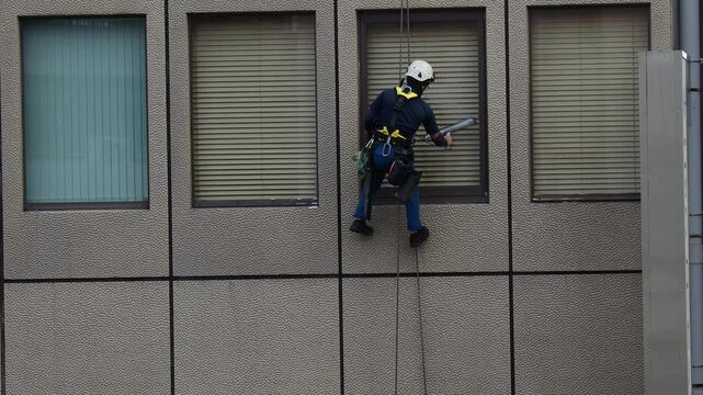 命綱を使って高層ビルの窓ガラスを掃除する作業員の姿