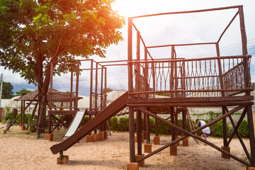 Children playground on sand yard activities in public park surrounded by green trees at sunlight morning. built climbing slide, seesaw on vintage playground.