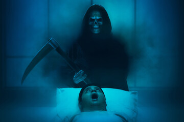 Silhouette of grim reaper with scythe and smoke mist fog kill man in bed, Halloween theme