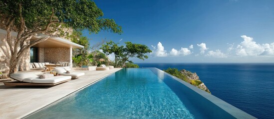 Fototapeta premium A luxurious infinity pool overlooking the ocean with lounge chairs and a stone wall.