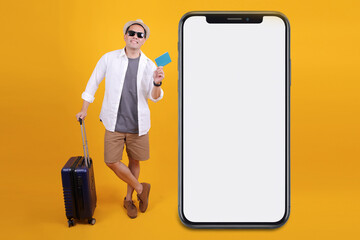 Cheerful Asian Traveler Man Showing Passport While Holding Suitcase With Huge White Blank Screen Smartphone
