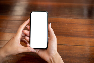 A close-up of a woman sitting at a wooden table indoors and using her smartphone.