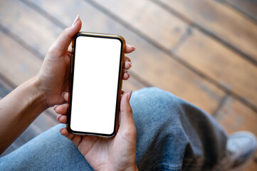 A woman's hand holding a smartphone with a white screen mockup while sitting on a terrace.