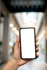 A woman's hand holding a smartphone, set against a blurred background of a market or mall.