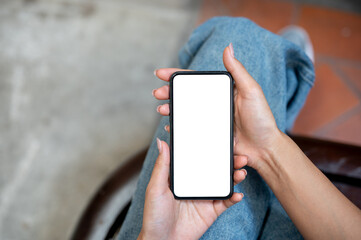 A top view of a woman in jeans sitting on a chair outdoors, using her smartphone.
