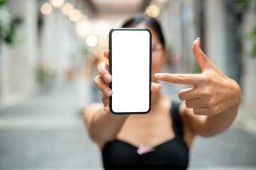 A woman pointing at a smartphone, showing it to the camera while standing in a market or mall.