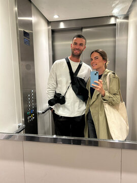 Couple take a selfie in the reflection of a mirror inside an elevator