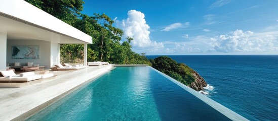 Fototapeta premium Modern infinity pool overlooking the ocean with lounge chairs and a white modern house in the background.