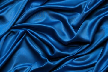 Fototapeta premium A close-up view of a deep blue satin fabric draped in soft, flowing folds. The smooth, luxurious texture is highlighted by the soft lighting.