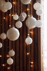A bunch of white Christmas balls of different sizes hanging on a rope against a background of brown curtains. New Year's decorations.