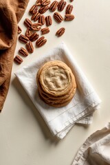 A napkin holds a stack of cookies above pecans and a piece of cloth.
