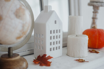 Cozy autumn decor featuring white house figurine and seasonal elements on a mantelpiece